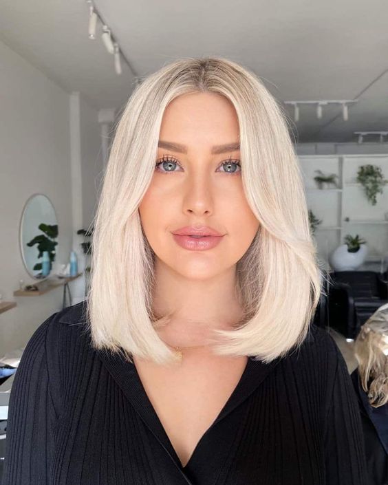 Medium length platinum blonde hair with a darker root, face framing layers and a lot of volume is a stylishidea
