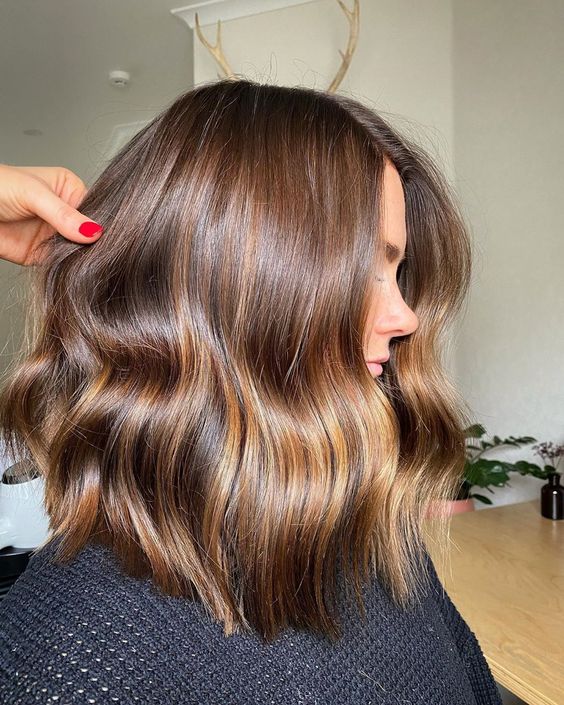 Medium length warm brown hair with gold blonde highlights and slight waves is a stylish and cool idea
