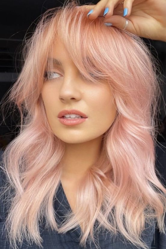 Peachy pink shoulder length hair with a lot of volume and waves and bottleneck bangs is a cool solution with a soft touch of color