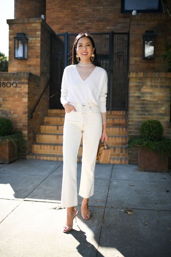 white flare jeans, a white top with a sheer shiny top underneath, strappy shoes and a brown mini bag plus statement earrings