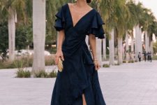 a beautiful and refined winter wedding guest look with a black maxi dress with an asymmetrical skirt, shiny shoes and statement earrings