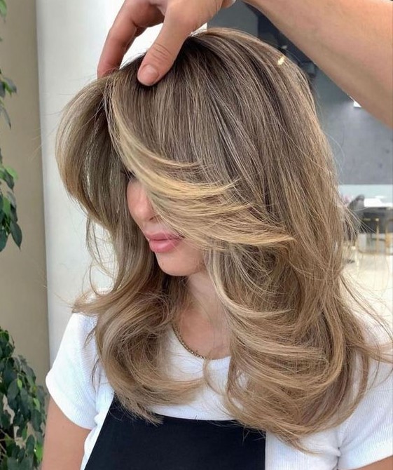 a beautiful medium butterfly haircut in bronde, with blonde highlights, with curved locks and side bangs is a cool idea