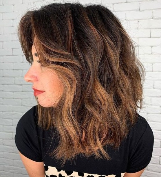 A black medium length haircut with caramel balayage and waves, with side bangs is a catchy and very chic idea