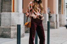 a bold and cool wedding guest look with a colorful printed top, burgundy velvet pants, white shoes and an amber bag