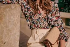 a bold floral wrap blouse with short sleeves, creamy high-waisted pants and a small bag are a cool combo for a casual summer wedding