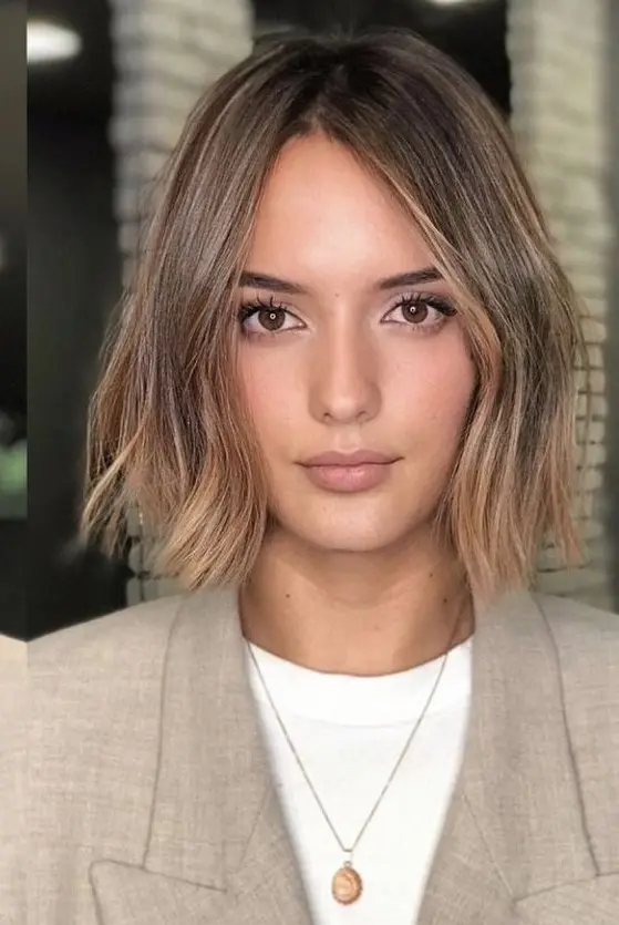 a brown bob with darker root and caramel and gold balayage, with irregular parting and slight waves