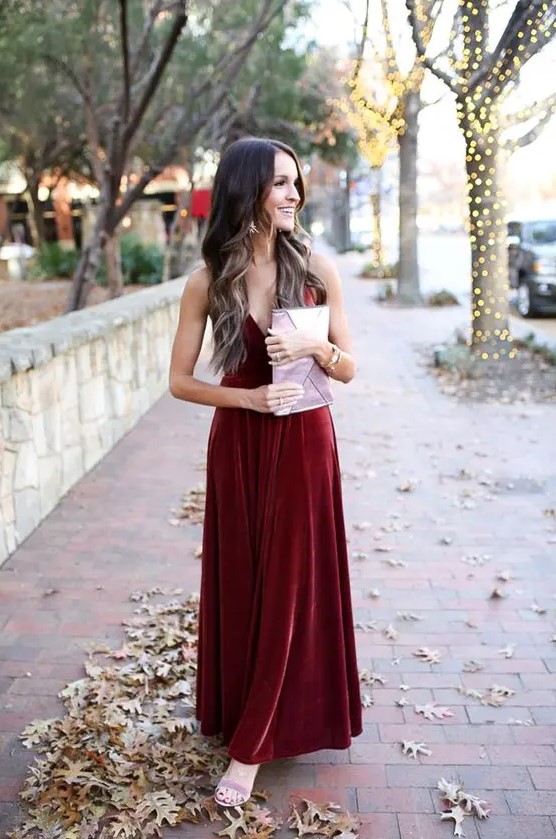 a burgundy velvet maxi dress with spaghetti straps, lilac shoes and a lilac clutch for a chic winter wedding guest look