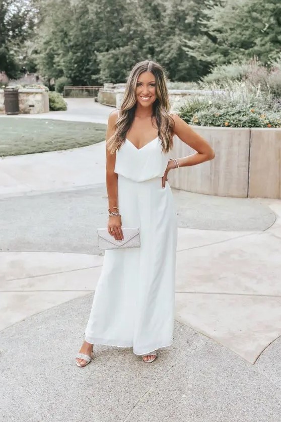 a casual bridal shower outfit with a white jumpsuit with spaghetti straps, neutral shoes and a silver clutch for summer