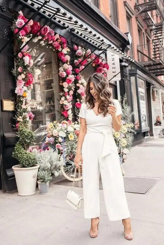 A casual white jumpsuit with a V neckline, short sleeves, wideleg pants, nude shoes and a white bag