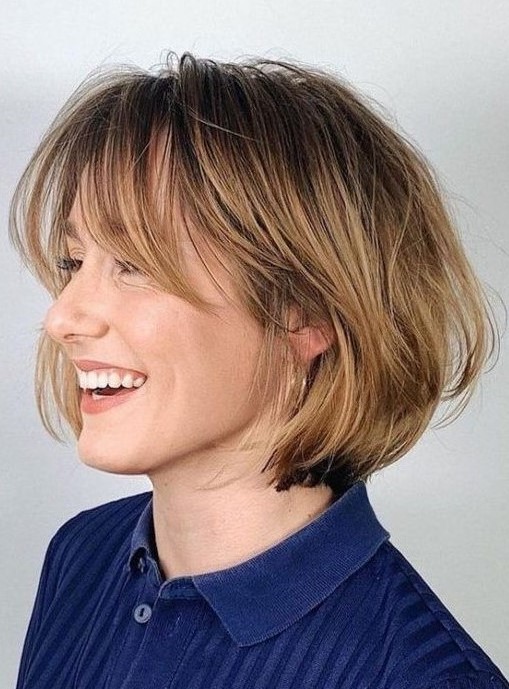 a chin-length bob with honey blonde balayage and long curtain bangs, curved ends and a bit of volume