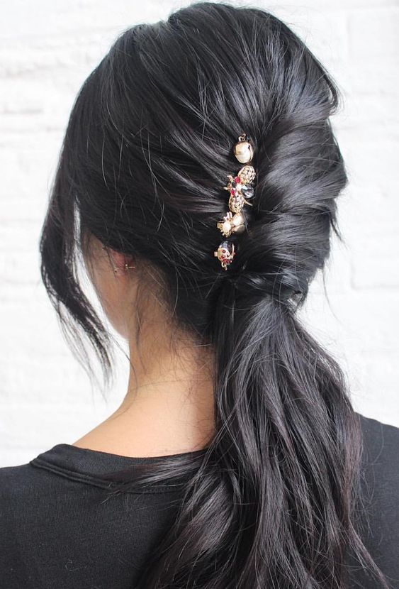 A classy black ponytail with a French chignon and embellished hair pins plus face framing hair