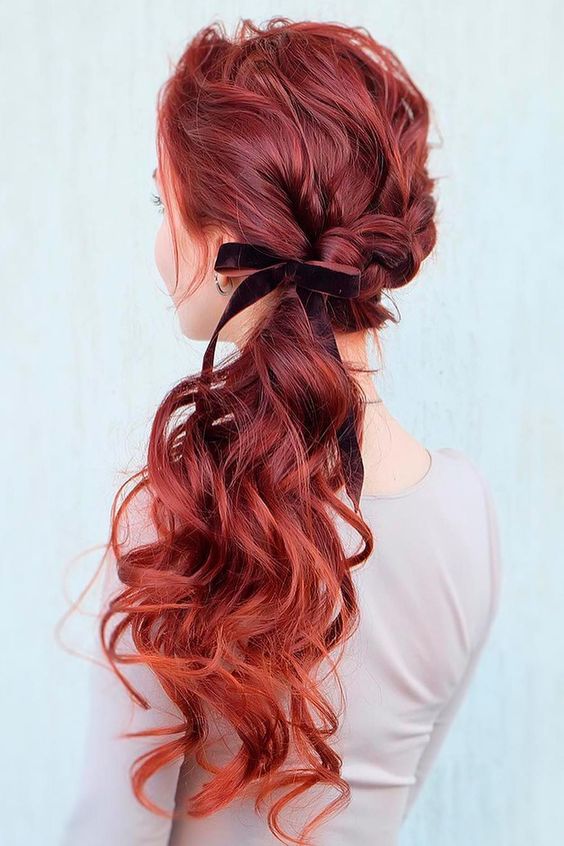 a curly low ponytail with a messy wavy top and a burgundy velvet bow is a cool and catchy idea
