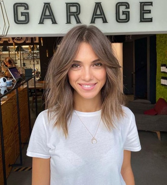 A light brunette shoulder length hairstyle with curtain bangs and messy texture looks shaggy and cool