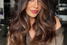 a long dark brown butterfly haircut with caramel balayage and waves on the ends, with a lot of volume, is a stunning solution