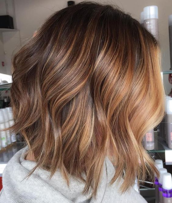 a long layered bob in brown, with caramel and golden blonde balayage including a chunky money piece and with volume and waves