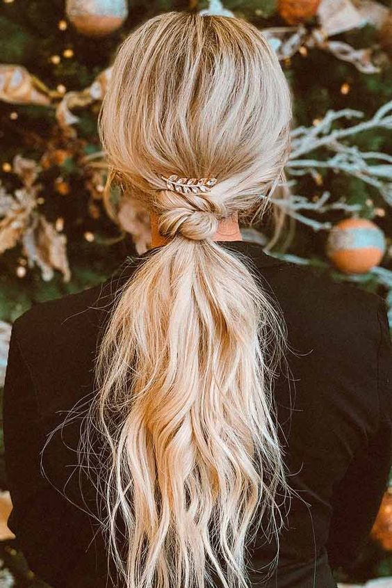 a long low ponytail with a twisted touch, messy wavy hair and a rhinestone feather as an accessory to the hairstyle