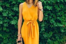 a marigold knee plain dress with thick straps, a sash, a whimsy printed bag and a watch for a casual summer wedding
