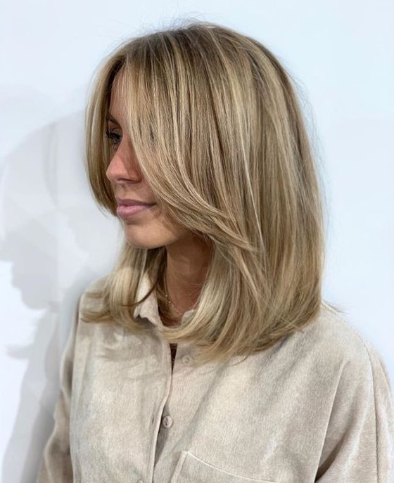 A medium length blonde hairstyle with long curtain bangs and blonde balayage is a lovely and chic idea