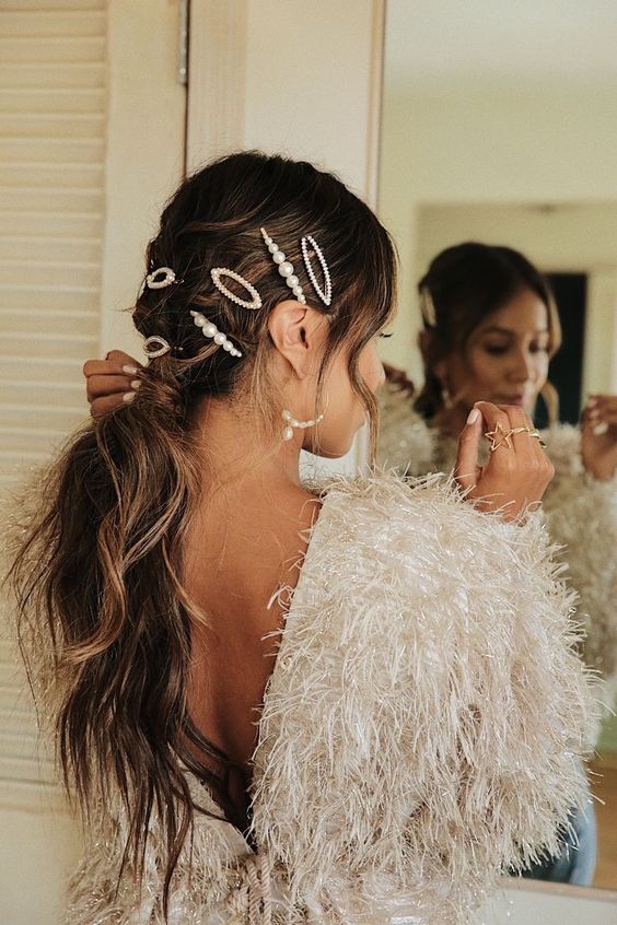 A messy and wavy low ponytail with a messy top and face framing hair, with pearl bobby pins is super cool