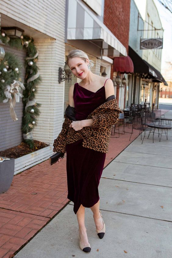 a pretty and chic winter wedding guest look with a burgundy velvet midi dress, two-tone shoes, a leopard cover up and a small clutch