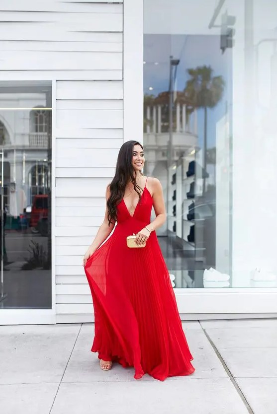 a red maxi dress with spaghetti straps, a deep neckline, a pleated skirt and nude shoes plus a neutral clutch