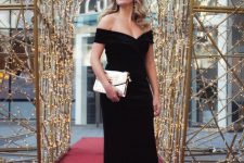a refined black tie wedding look with a black off the shoulder maxi dress, red shoes and a metallic bag