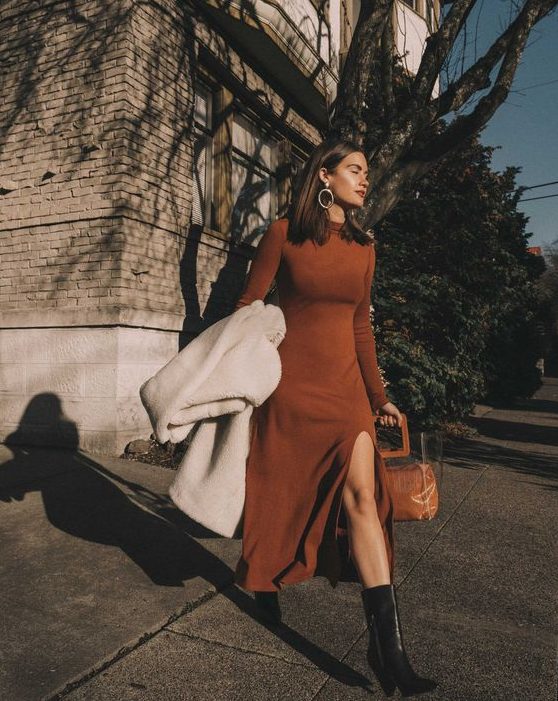 A rust midi A line knit dress with long sleeves, a slit, a turtleneck, black cowboy boots and a white faux fur coat