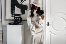 a slip midi dress, a white sweater over it, white shoes, a hat and a large clutch for a winter bridal shower