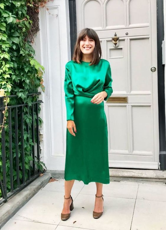 a stylish and simple winter wedding guest look with an emerald midi satin dress with a draped bodice and long sleeves and brown shoes