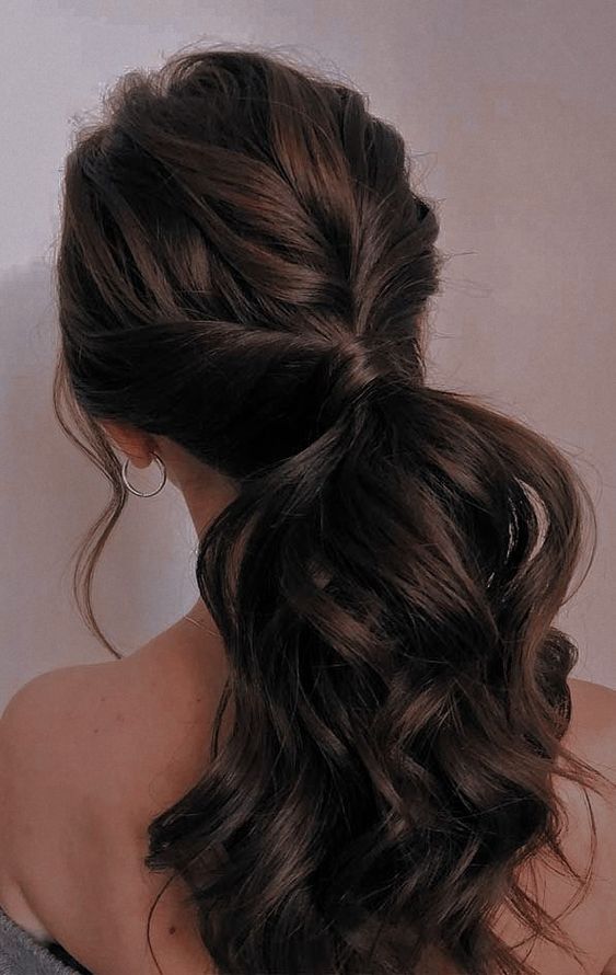 a volumetric low ponytail with a twsited top and waves down is a chic and cool idea to rock right now