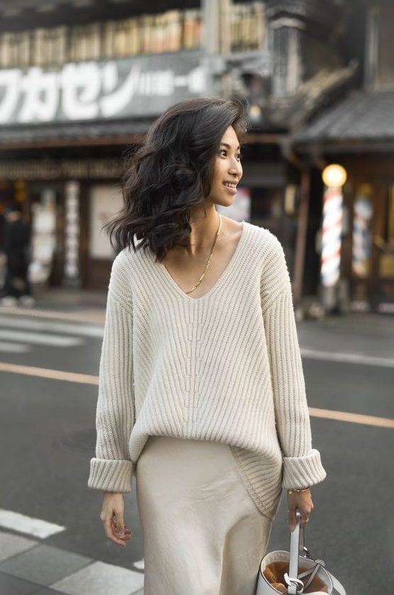 An oversized chunky creamy sweater with a V neckline, a neutral slip skirt and a bucket bag for a feminine look