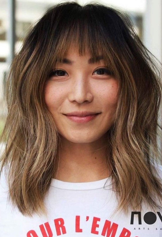 Dark brunette medium length hair with caramel balayage and ombre, wispy bangs and slight messy waves is a cool idea