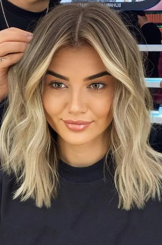 Medium length blonde hair with a shadow root and slight waves is a cool idea, it looks stylish and chic