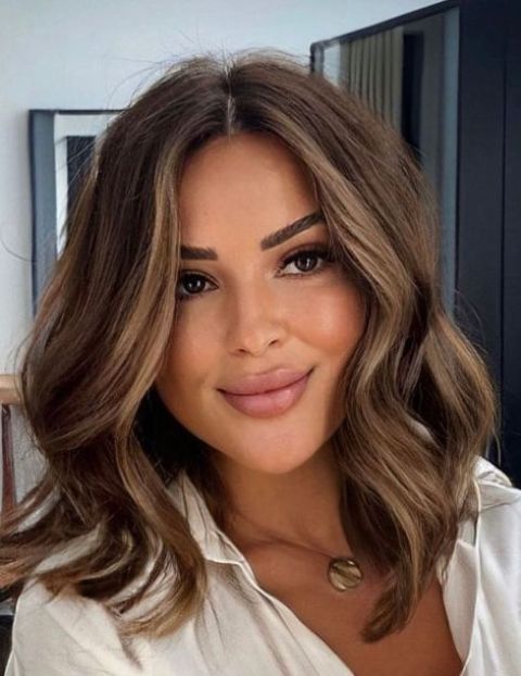medium-length brunette hair with slight caramel highlights and face-framing layers, waves and volume