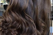 very long and extra volumetric dark brownn hair with golden blonde balayage that brings dimension and curls on the ends