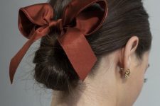 a chic and feminine twisted low bun with a sleek top and a burgundy ribbon bow for an elegant look