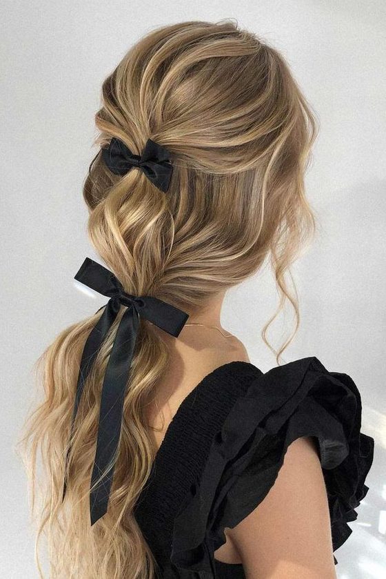 a chic and refined ponytail with waves and a bump on top plus a couple of black bows is wow