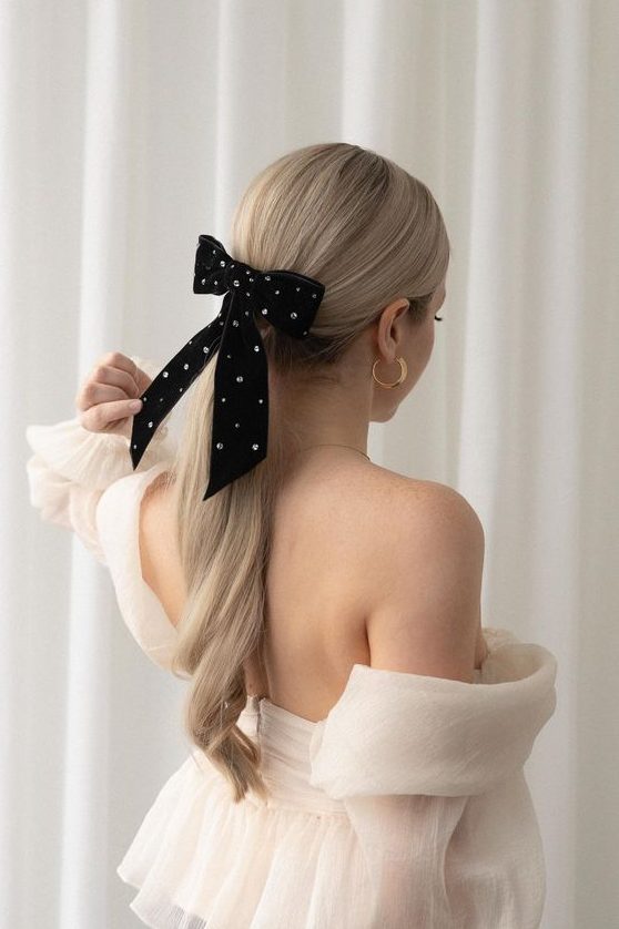 a classy curled low ponytail with a sleek top and an embellished black velvet bow is amazing