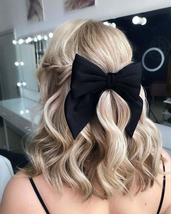 a glam and pretty half updo with twists, waves and a black bow is a cool and catchy idea