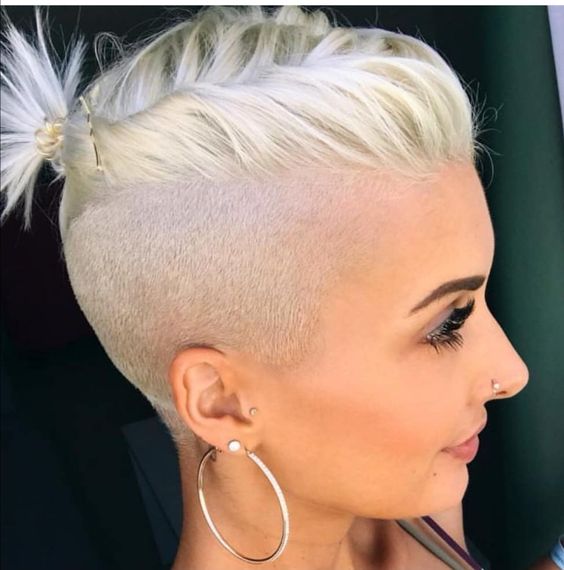 a long bleached blonde pixie with an undercut styled with a little ponytail on top to keep the hair off the face