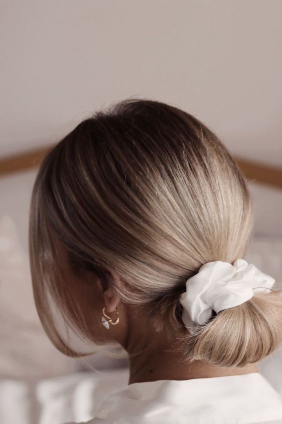 a lovely low updo with a sleek top and a low bun made with a scrunchie and face-framing hair