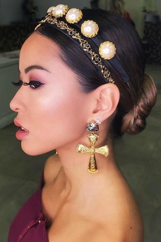 a low bun with a sleek top accented with a headband with chain and large pearls, with bold and statement earrings for the holidays