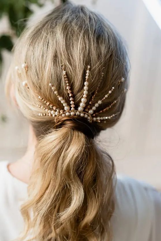 a low wavy ponytail with a bold rhinestone and pearl hair piece is a stylish idea to rock