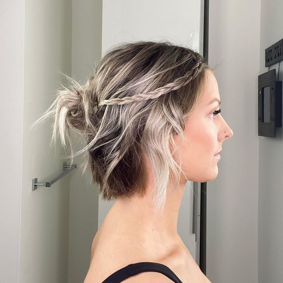 a messy and casual half updo with a messy top knot and a braid plus waves down