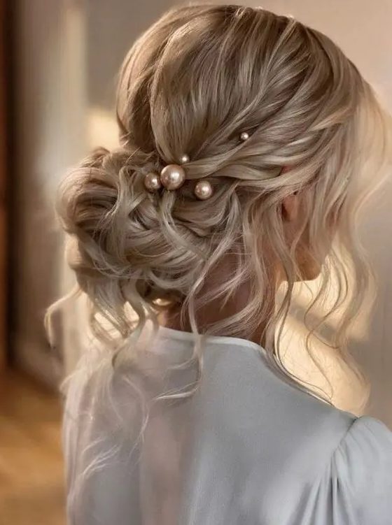 a messy wavy low bun with a wavy top, some locks down and face-framing hair plus some large pearl hair pins