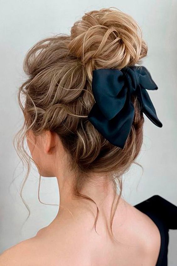 a pretty messy and wavy top knot with a wavy top, some locks down and a black bow for an accent