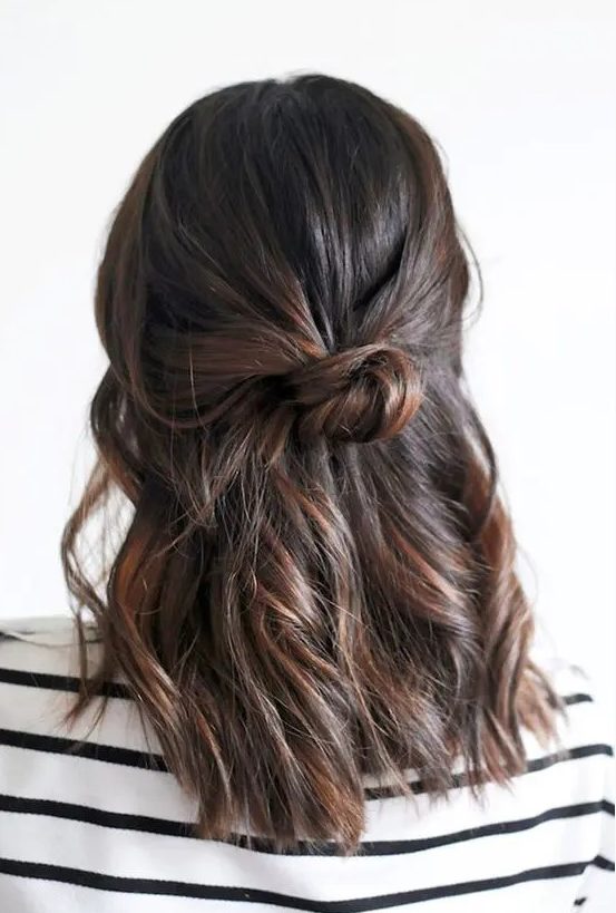a simple half updo with a textured top, waves down and a bun is a cool idea for a bridesmaid