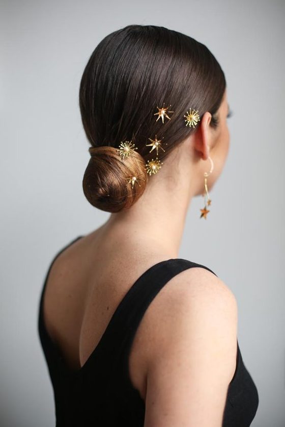 a very sleek and chic low bun with a sleek top and gold star hair pins is amazing for a refined holiday look