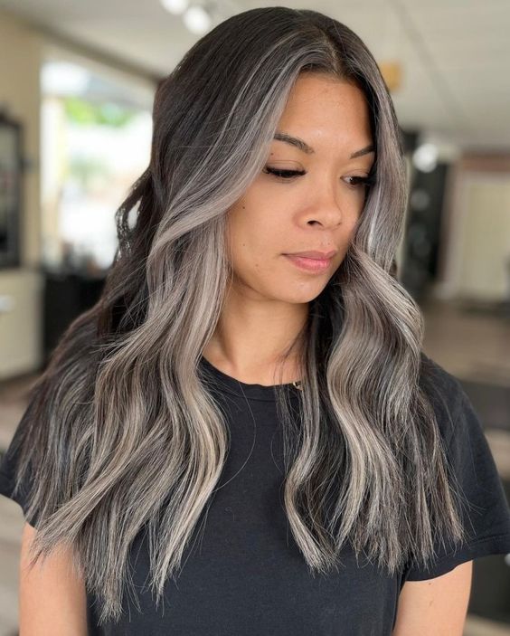 long wavy black hair with a grey money piece and some more greys naturally blended in