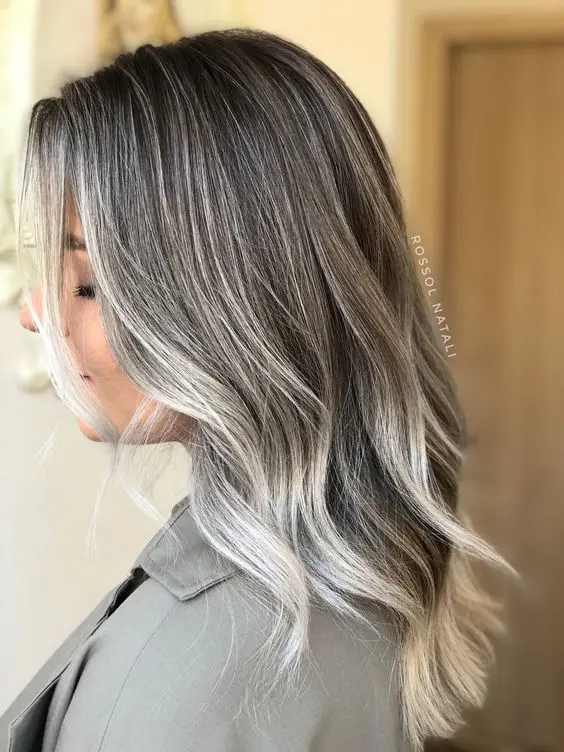 Medium length dark hair accented with silver greys and with matching money piece, with waves, is a lovely idea to transition to grey
